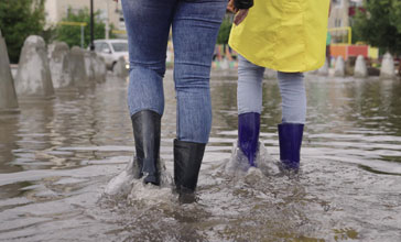 girls in raincoats and rubber boots walk along flooded road