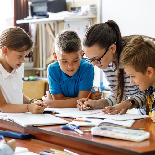 Female teacher helps school kids to finish their tasks