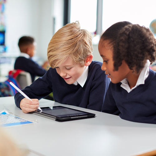 Primary school kids sitting together at desk using a tablet
